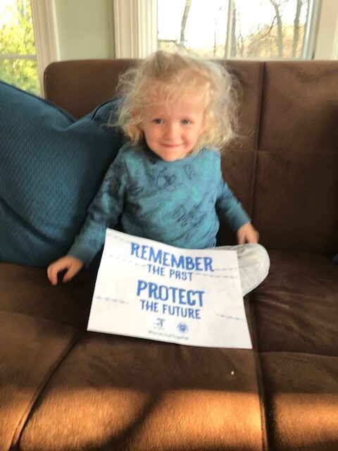 A little girl sitting on the couch holding a sign.