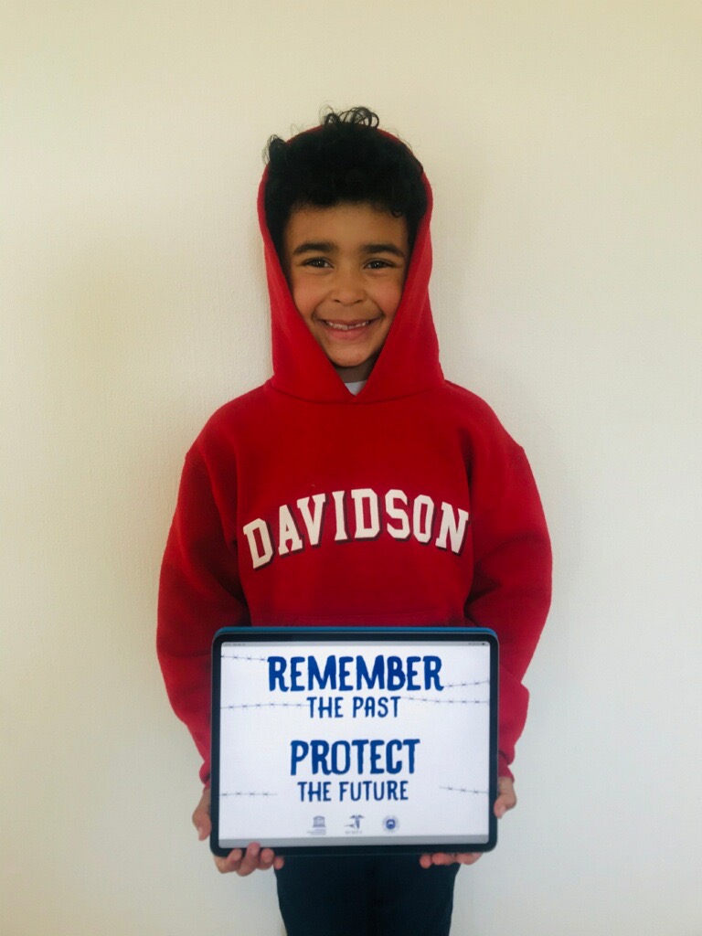 A young boy holding up a sign that says " remember the first protect the future ".