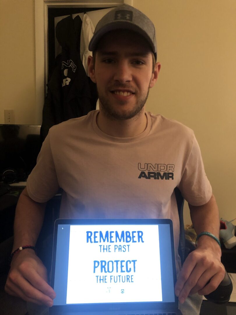 A man holding up a laptop with the words " remember, we must protect ".