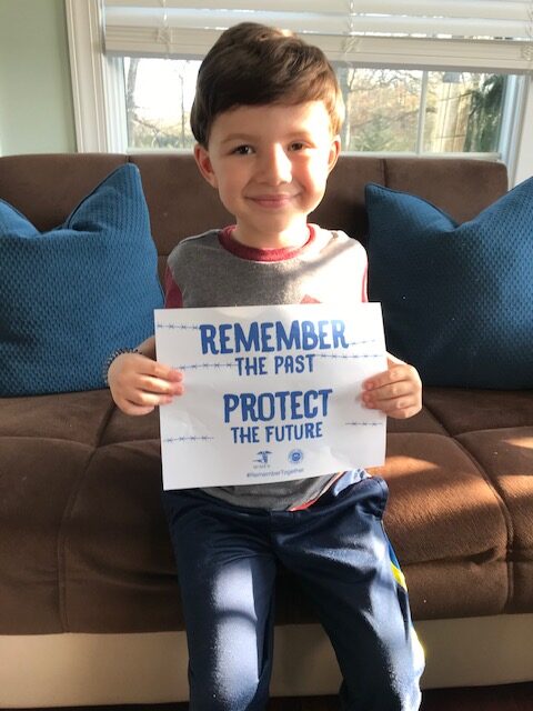 A young boy holding up a sign that says " remember the past protect the future ".