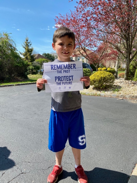 A young boy holding up a sign that says " remember to take this photo protect the trees ".