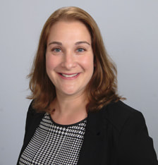 A woman in black jacket and white shirt smiling.