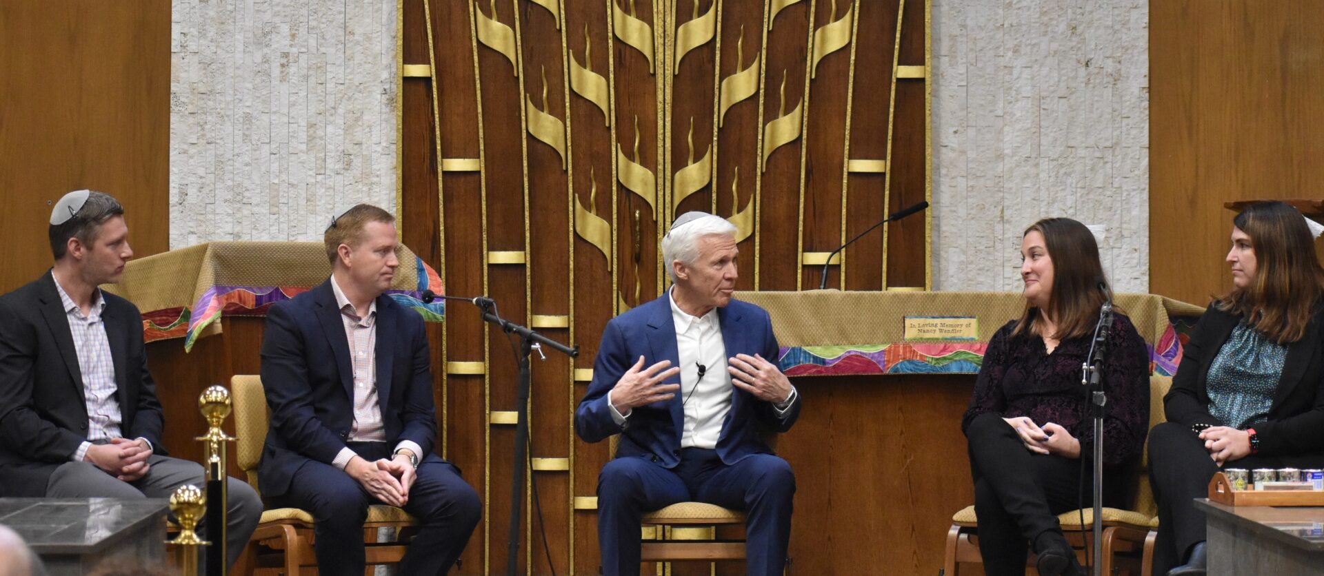 Two men sitting in front of a wooden wall.