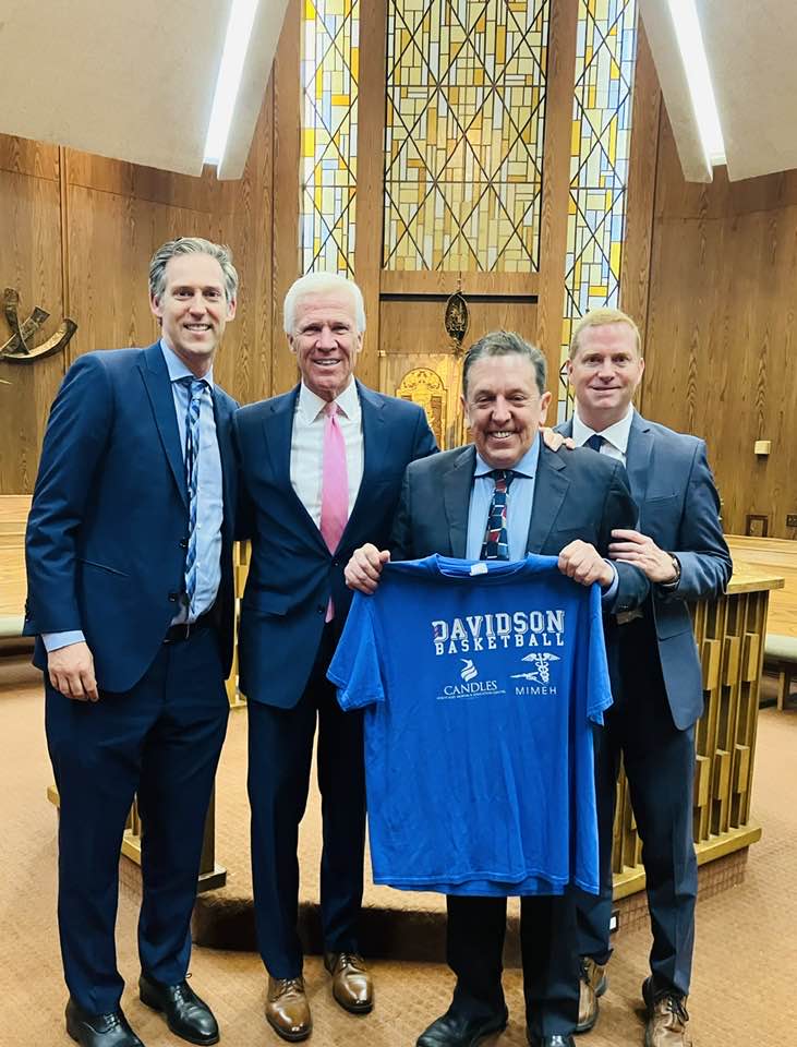 Four men in suits and ties holding a blue shirt.